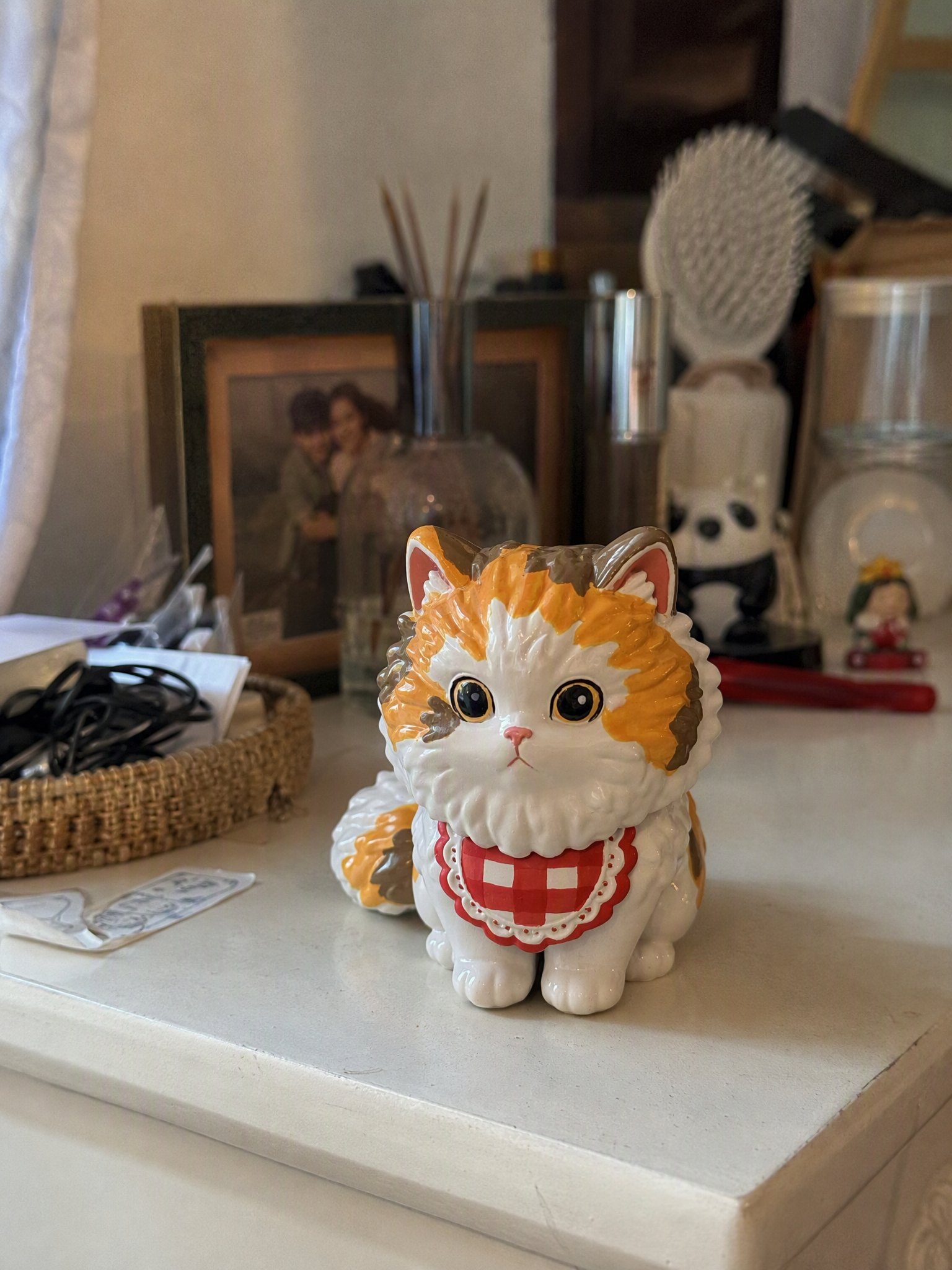 A hand-painted chibi cat figurine on a dresser beside framed photos and keepsakes