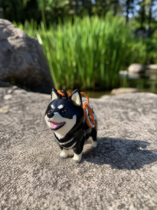 Hand-painted chibi black shiba keychain standing on a rock by a pond